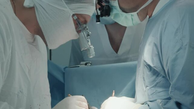 Surgeon holds thread with micro forceps. Experienced surgical team attaches grafted vessels on artery to divert blood supply in operating room
