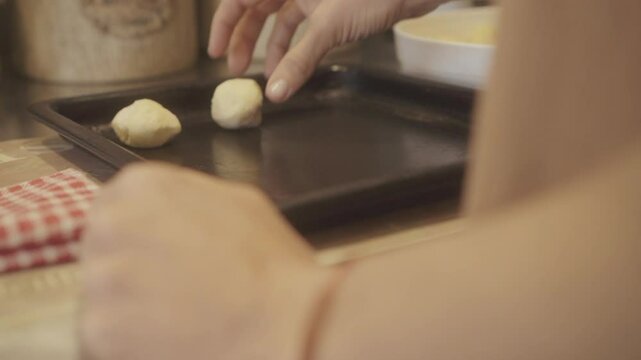 Hands preparing traditional chipa bread on a baking tray in a cozy kitchen, showcasing the process of making and enjoying this beloved treat at home