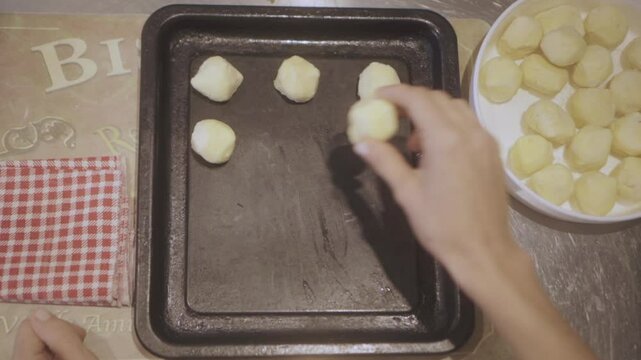 Close up overhead footage of hands forming dough balls for chipa bread on a baking tray, showcasing the traditional baking process at home