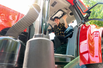 Female farmer sitting in tractor cabin smiling and waving. Woman driving agricultural or...