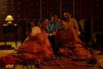 Cheerful senior woman capturing moments of Diwali celebration with her husband and friends over mobile phone