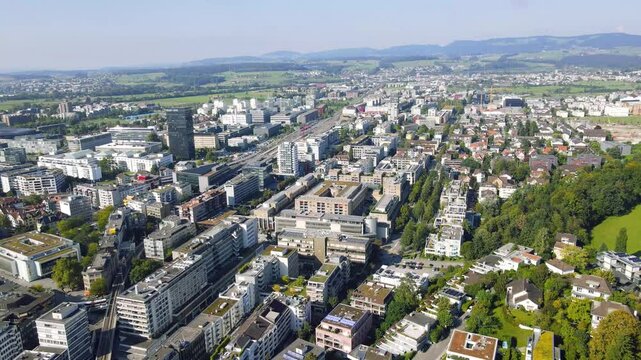 Panoramic drone shot of the city of Zug in Switzerland with its central train station visible in the distance and surrounded by the lush green hills of the Swiss countryside
