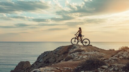 Fototapeta premium A woman stands isolated on a rocky precipice with her bike, taking in the expansive view of the serene ocean below during twilight.