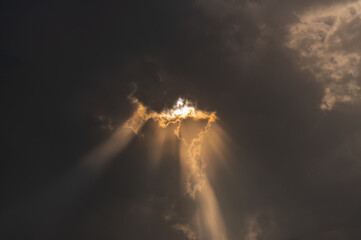 Sun rays coming out from the dense black rain clouds which makes beam of light rays and highlights the edge of clouds.