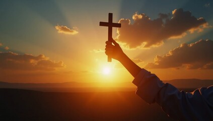 A person holding a cross in front of a sunset.