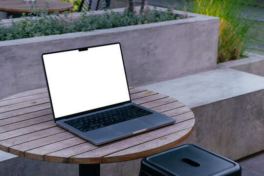 Mockup image of laptop with blank white desktop screen on wooden table in outdoor cafe.