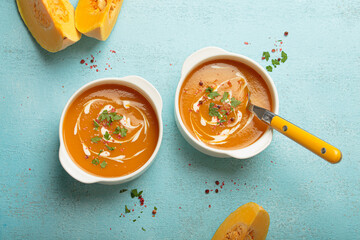 Creamy pumpkin soup bowls on blue background with parsley and pink pepper, a cozy autumn meal option