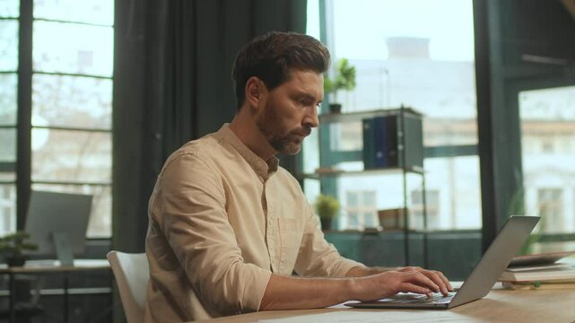 Attractive worker man sitting at desk use laptop typing on keyboard in the office. Serious businessman. Camera moving around. 360 Degree