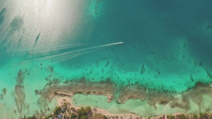 Aerial top down view speedboat leaving white trail on turquoise crystal water lagoon, boat riding across coral reef line shore. Tropical island beach. Perfect exotic summer travel vacation background