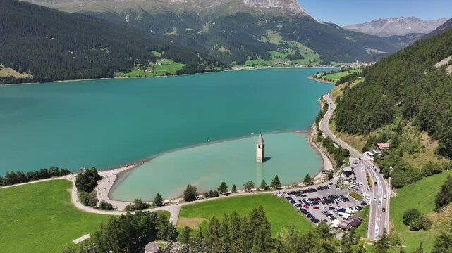 The famous bell tower in Italy with a mountain backdrop and surrounding area, road, and vehicles, Curon, Italy