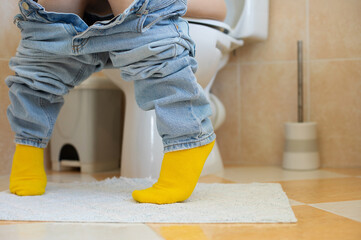 A close-up of a person sitting on a toilet with jeans pulled down and wearing bright yellow socks....