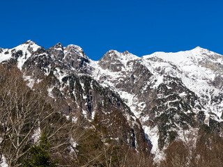 A majestic mountain range dominates the horizon, its peaks dusted with snow under a clear blue sky.