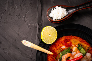 tom yum kung Spicy Thai soup with shrimp in a black bowl on a dark stone background, top view, copy space