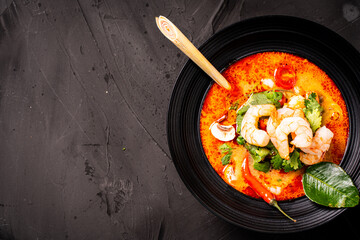 tom yum kung Spicy Thai soup with shrimp in a black bowl on a dark stone background, top view, copy space