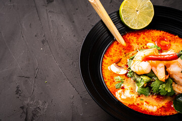 tom yum kung Spicy Thai soup with shrimp in a black bowl on a dark stone background, top view, copy space