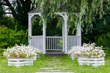 idyllic spring time park lawn symmetry wooden painted in white gazebo frame work with flower pots on both sides peaceful natural environment space with focus on foreground