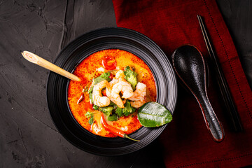 tom yum kung Spicy Thai soup with shrimp in a black bowl on a dark stone background, top view, copy space