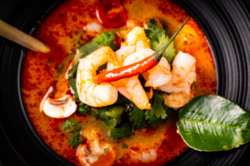 tom yum kung Spicy Thai soup with shrimp in a black bowl on a dark stone background, top view, copy space