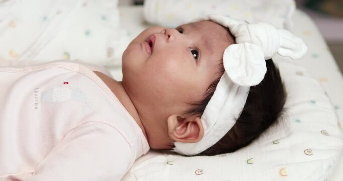 Stretching her legs and arms as she moves from side to side, a newborn baby is also rubbing her eyes and showing a little smile on her chubby face.