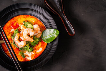 tom yum kung Spicy Thai soup with shrimp in a black bowl on a dark stone background, top view, copy space