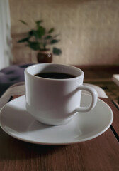 White cup and saucer with hot coffee on rustic background in room. vertical photo