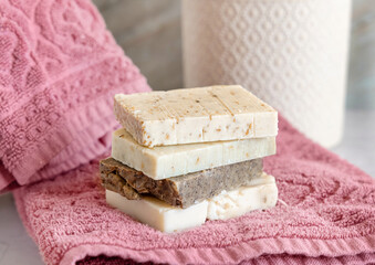Handmade beige soap bars on pink folded towels near potted plant in bathroom close up