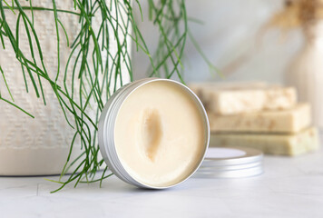 Opened body butter jar on marble countertop near green plant close up, cosmetic mockup