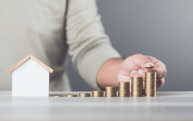 Man is stacking coins on a table, arranging them from smallest to largest, with a wooden house...