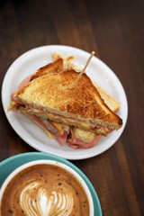 Toasted ham and cheese sandwich and large cup of coffee on a bar table. Red bowl with heart-shaped latte art. Hot drink. Coffee with milk. Cappuccino.