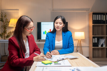 Two women in suits are sitting at a table with papers and a projector