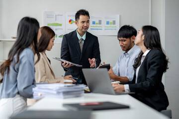 A group of people are sitting around a table with laptops and papers