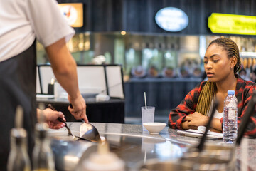 Happy young woman enjoying teppanyaki chef cooking meal in front of her at a japanese restaurant, smiling customer interacting with chef, traditional asian cuisine, live cooking experience, fresh food