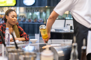 Happy young woman enjoying teppanyaki chef cooking meal in front of her at a japanese restaurant, smiling customer interacting with chef, traditional asian cuisine, live cooking experience, fresh food