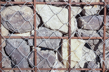 A close-up view of a gabion wall, featuring rough, natural stones encased within a metal grid structure. The stones vary in size, shape, and color, providing a rugged and industrial look. backgrounds 