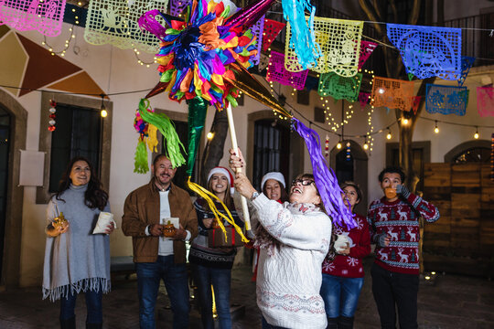 Mexican woman and family breaking a pi&ntilde;ata at traditional posada party for Christmas in Mexico Latin America, hispanic people