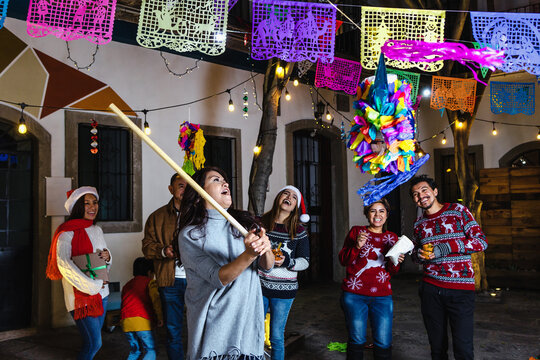 Mexican woman and family breaking a pi&ntilde;ata at traditional posada party for Christmas in Mexico Latin America, hispanic people