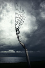 Moderne Metallskulptur vor stürmischem Himmel am Meer