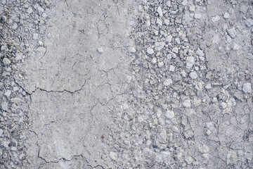 close-up of a textured dry soil surface with small stones or gravel scattered on a light gray ground