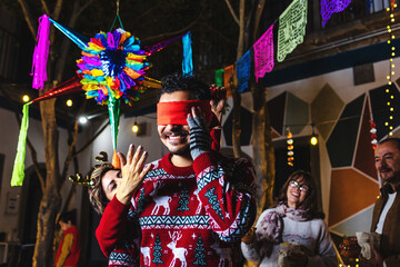 mexican man breaking a pinata at traditional posada celebration for Christmas eve in Mexico Latin America, hispanic family in holidays