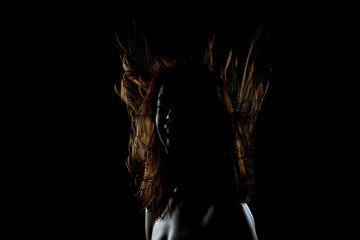 This striking image captures the silhouette of a woman with her hair dramatically lit and flowing, set against a dark background, evoking emotion and mystery.