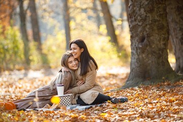 Two girls making picnic on a blanket in autumn park