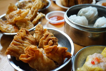 Traditional Chinese dim sum in metal bowl on wooden table. A lot of different kinds of food and drinks on the table