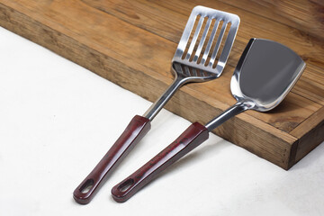 Two types of cooking spatulas, both frying and stir-frying, are placed ready to use on a wooden cutting board on a white floor in the kitchen