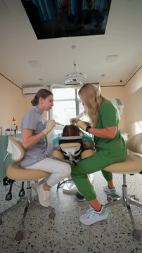 Blonde Woman Dentist with Assistant Treat Teeth Female Patient with Special Instrument. Treatment Caries and Plaque in Dental Clinic. Concept of Medicine and Healthcare. Vertical Video. Slow Motion.