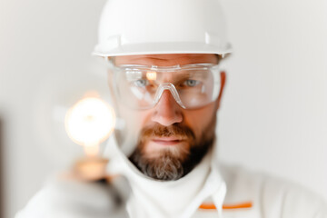 The construction worker, equipped with safety goggles and a hard hat, confidently holds a spotlight in a bright, organized work area, promoting safety awareness