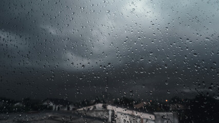 Raindrops on the window glass. The overcast sky is full of dark clouds and a storm is coming. Rainy season. Meteorology and weather forecast.