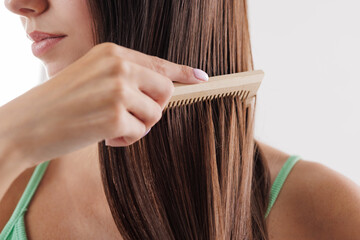 Close up of a woman combing her long straight brown hair with a wooden comb. hair care