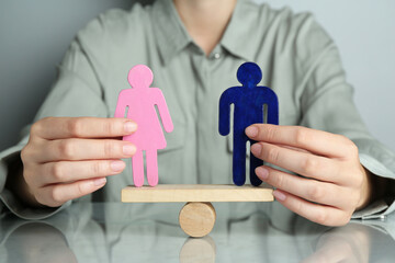Gender equality concept. Woman with male and female figures on scales at grey table, closeup
