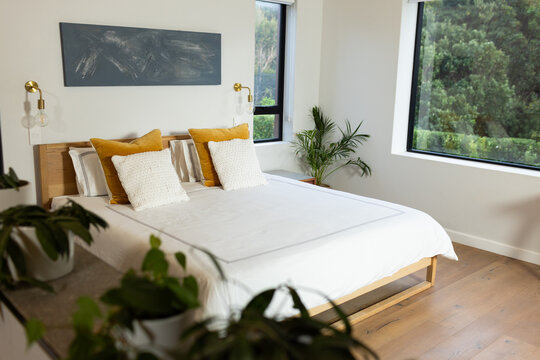 Modern bedroom with white bedding, yellow pillows, large windows overlooking greenery, copy space