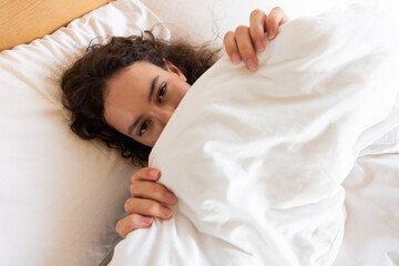 Relaxing in bed, woman peeking from under white blanket, enjoying spa day